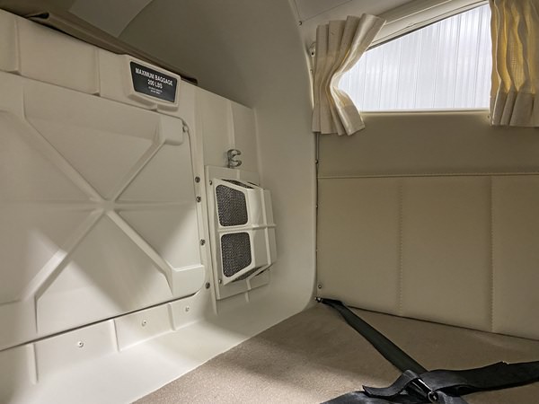 Inside a Piper Aire aircraft showing a warm air inlet in the air conditioning unit, with beige and tan walls, and a window with an open curtain.