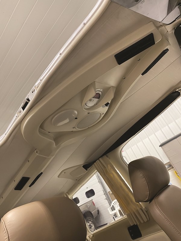 Overhead console of the interior of a Piper Aire aircraft, with beige seats and roof, and windows with open curtains.
