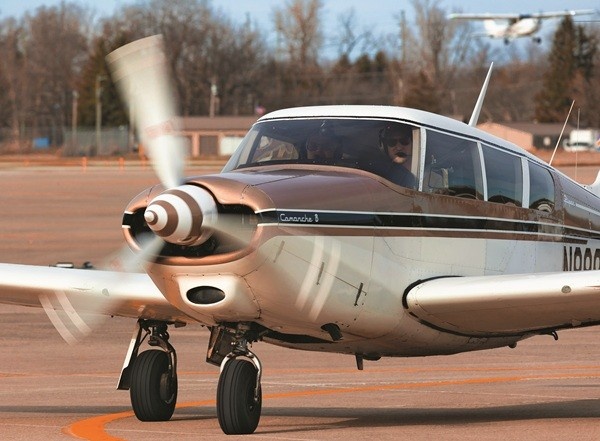 Close-up of the front end of a white and light brown Piper PA-24-260 Comanche 260B aircraft with the motion blur of its spinning propeller.
