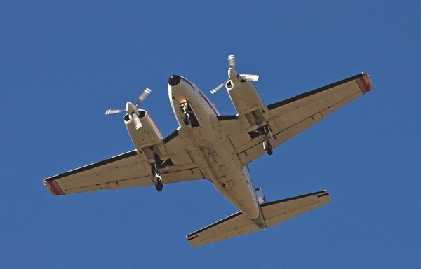 A Piper PA-31-310 Navajo flying directly overhead, showing its underside against a clear blue sky.