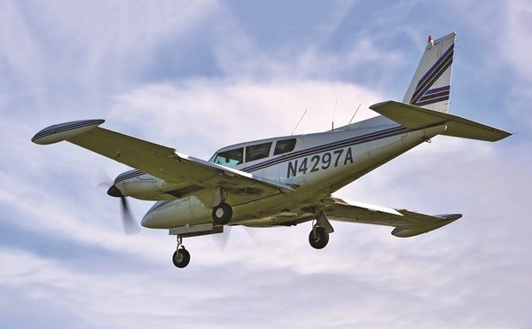 Underside view of a Piper PA-39-160 Turbo Twin Comanche C/R aircraft with the tail number N4297A as it soars through blue skies and white clouds.