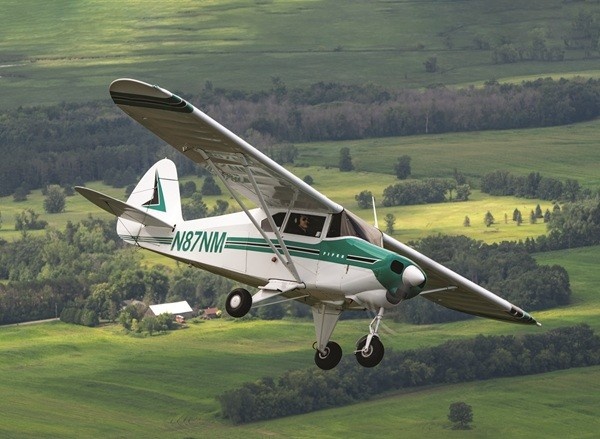 Piper Short Wings: Short on Wing Span Long on Fun A vintage white and green Piper Tri-Pacer light aircraft with the tail number N87NM flies over green countryside.