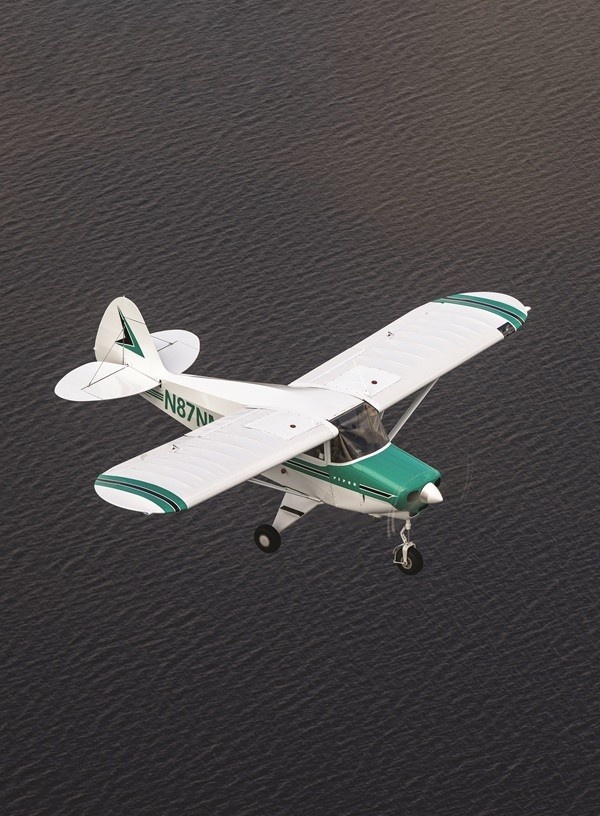 Bird's eye aerial view of a vintage white and green Piper Tri-Pacer aircraft flying over a large body of water.