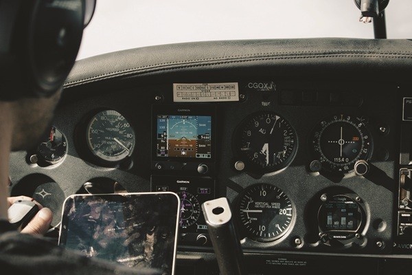 Pilot holding a tablet sits in front of a black Piper aircraft cockpit panel displaying pilot instruments, gauges, and Garmin avionics.