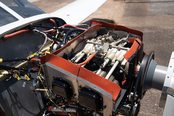 Continental aircraft engine installed in a parked Piper with the cowling removed, showing internal wiring, hoses, and red baffles.