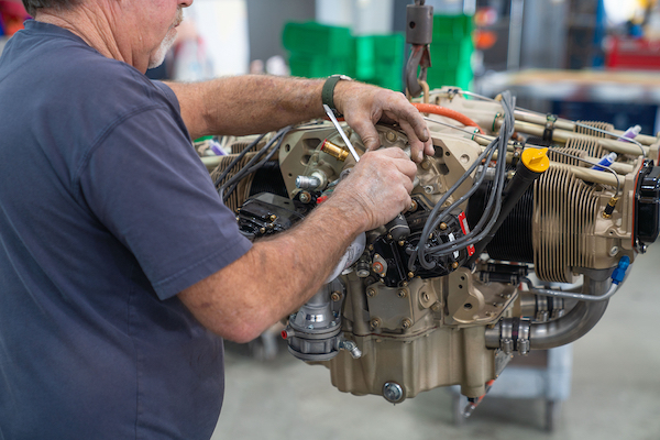 A technician uses a tool to perform maintenance on a detached, gold-colored Continental aircraft engine assembly.