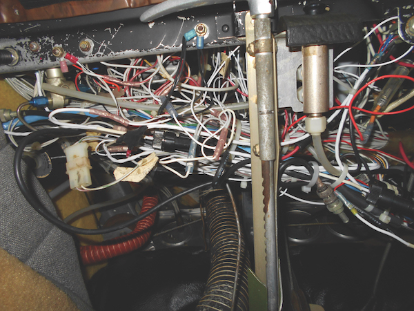 View behind a cockpit panel showing many intertwined white, red, and black avionics wires on a Piper aircraft.
