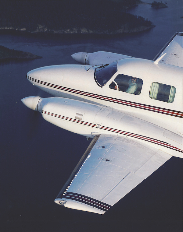 Aerial view of a white modified twin-engine Piper PA-31 Navajo aircraft flying over water, showcasing vortex generators on the wings.