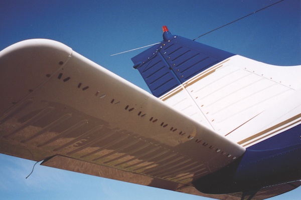 Low angle view of an aircraft's blue and white tail section, showing vortex generators lining the horizontal stabilizer.