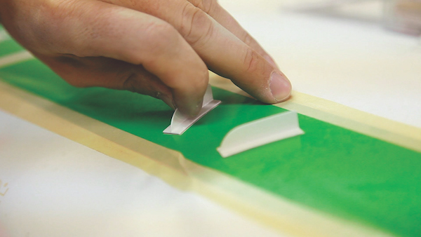 Close-up of a person's hand precisely placing a small, white vortex generators onto a green alignment template.