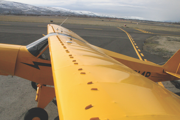 View looking down the bright yellow wing of a parked aircraft, showing a row of installed vortex generators.