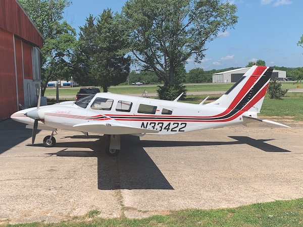 Profile view of a white Piper aircraft with red and black stripes and tail number N33422 parked outside a hangar on a sunny day.